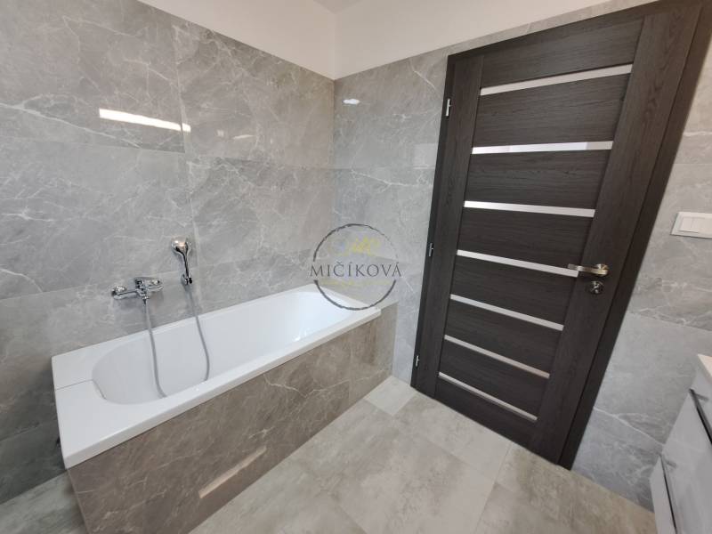 Ein Badezimmer in einem Einfamilienhaus mit einer Badewanne, grauen Fliesen und dunklen Türen.