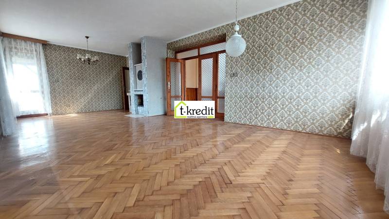 Ein geräumiges Zimmer mit Holzboden und gemusterten Tapeten in einem Einfamilienhaus.