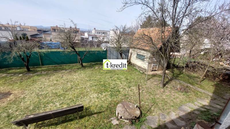 Der Garten des Einfamilienhauses in Zlaté Moravce mit Rasen, Bäumen und einer Bank.