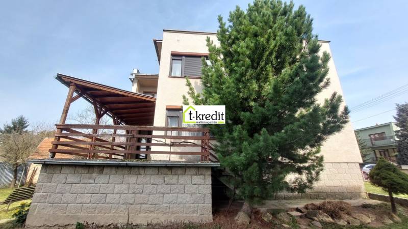 Ein Einfamilienhaus in Zlaté Moravce mit einer Holzterrasse, einem hohen Baum und einem Garten.