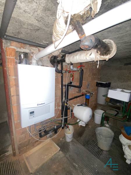 Ein Gaskessel im Keller eines Einfamilienhauses mit Rohrleitungen und einem Wasserspeicher an der Wand.