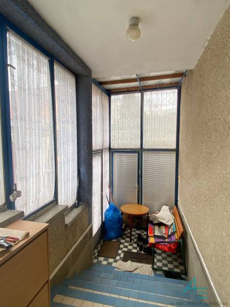 Veranda mit Glaswänden und blauen Rahmen, Schachbrettboden und einfache Möbel.