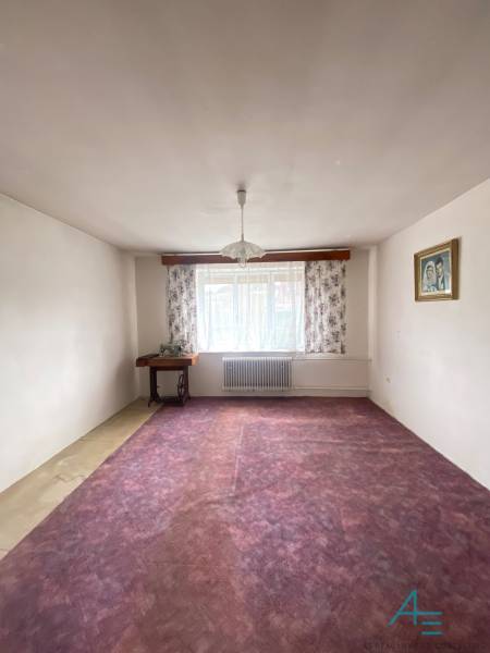 Ein Zimmer in einem Einfamilienhaus mit einem violetten Teppich, Blumenvorhängen und einem Kronleuchter.