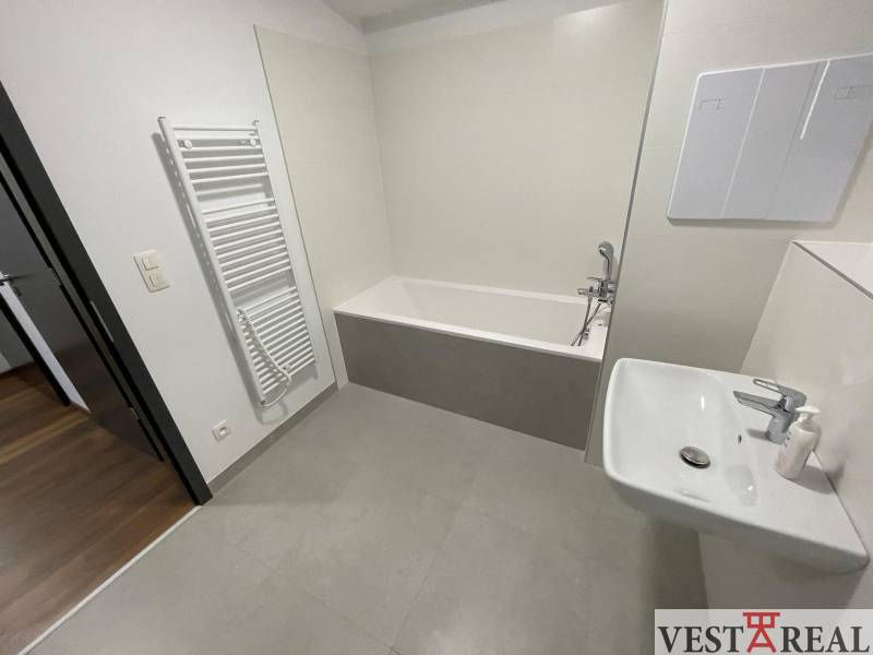 Badezimmer einer 2-Zimmer-Wohnung, Novomestská Straße: Badewanne, Heizkörper, Waschbecken, Eingang auf Holzboden.