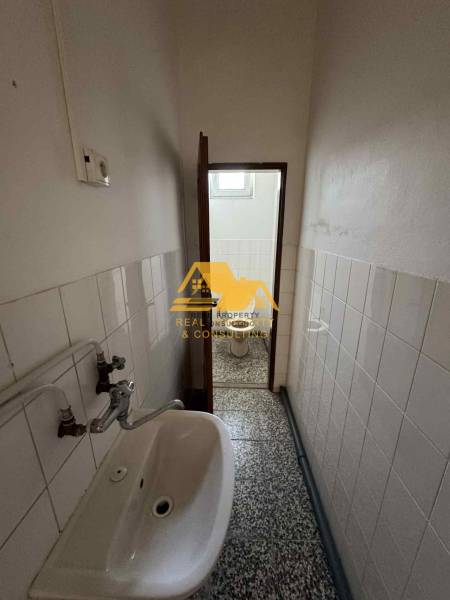 Einzimmerwohnung mit engem Badezimmer mit Waschbecken und Toilette, gefliest mit weißen Fliesen.