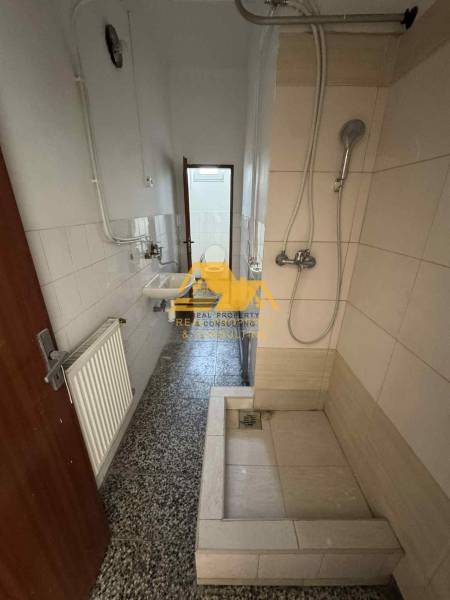 Badezimmer in einem Studio-Apartment mit einer einfachen Duschkabine, einem Waschbecken und Fliesen.