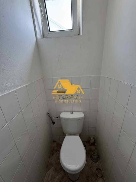 Kompakte Toilette mit Fenster, weiße Fliesen, Boden mit Holzdekor.