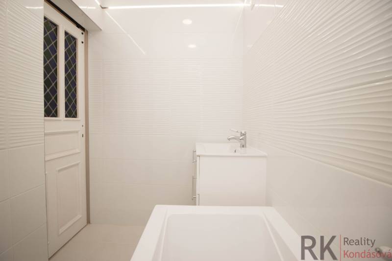 Badezimmer in einer 2-Zimmer-Wohnung mit weißen Fliesen, Waschbecken und Badewanne.