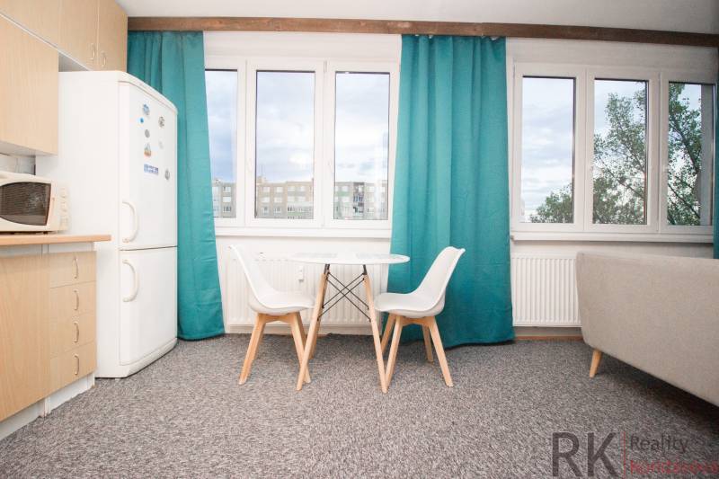 Küche mit Tisch und Stühlen in einer 4-Zimmer-Wohnung, Schrank und Fenster mit türkisfarbenen Vorhängen.