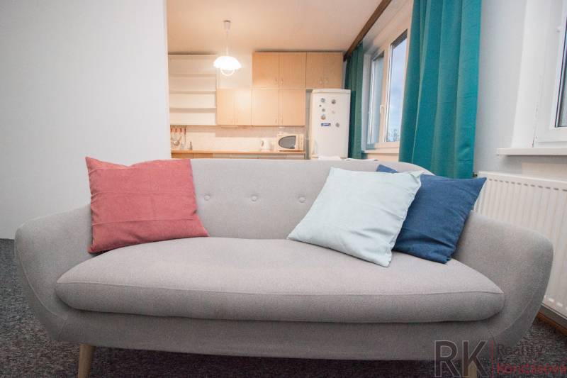 Ein graues Sofa mit bunten Kissen in einer Vierzimmerwohnung am Fenster und in der Nähe der Küche.