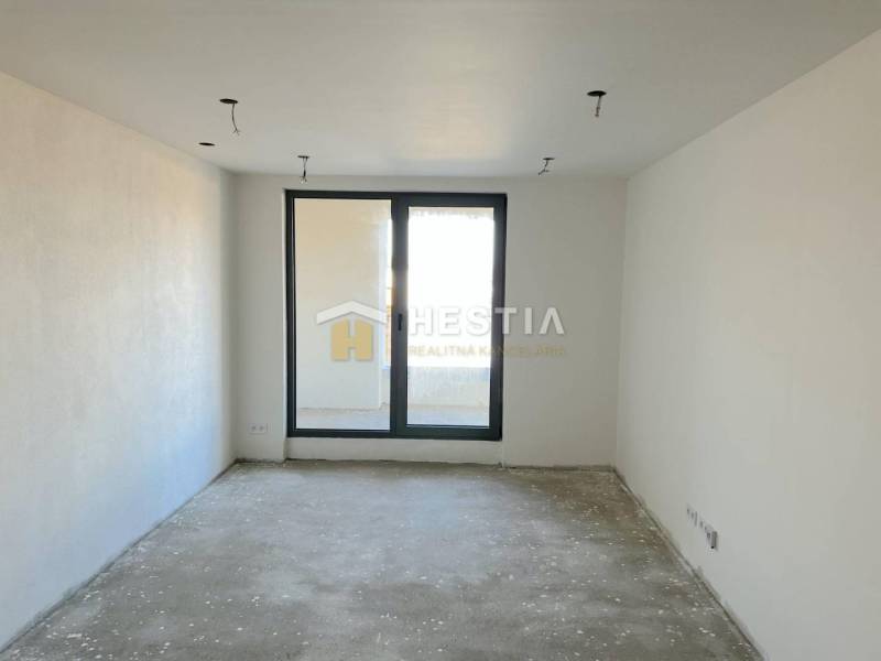 Ein leerer Raum mit Betonboden, Blick auf den Balkon und einem großen Fenster, geeignet für eine 2-Zimmer-Wohnung.