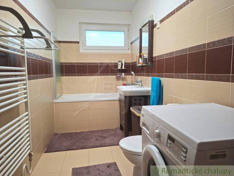 Badezimmer im Einfamilienhaus mit Badewanne, Waschmaschine und braun-beigen Fliesen.