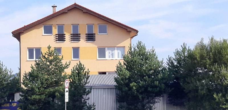 Das gelbe Haus mit dem schrägen Dach und den Fenstern hinter den Bäumen in der Nähe der Bürogebäude.