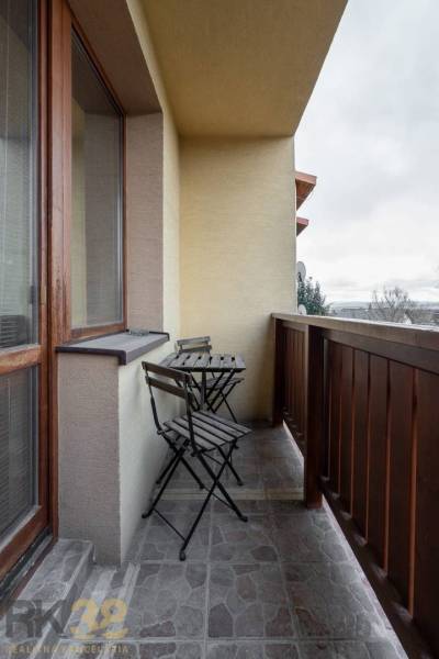 Ein Balkon mit einem hölzernen Geländer und einem Tisch mit zwei Stühlen in einer Wohnung mit fünf oder mehr Zimmern.