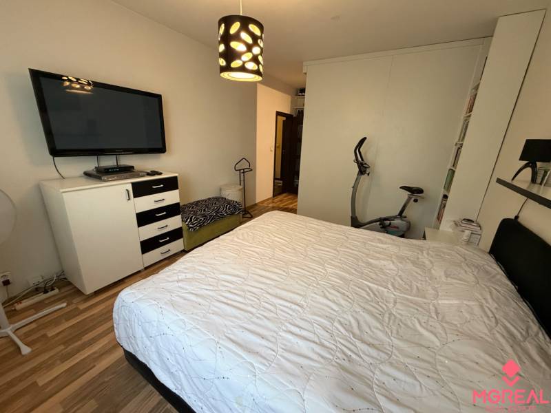 Schlafzimmer in einer 3-Zimmer-Wohnung mit Bett, Fernseher und Boden mit Holzdekor.