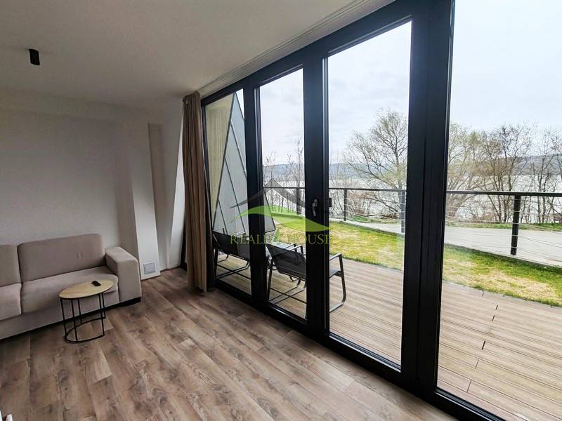 Innenraum der Hütte mit Sofa, Holzboden, große Fenster mit Blick auf die Terrasse.