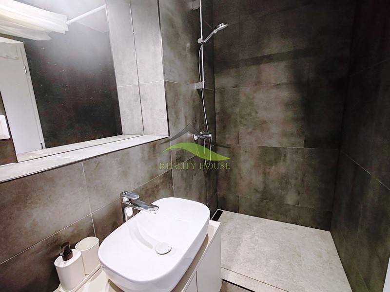 Ein Badezimmer in einer Hütte mit Waschbecken, Spiegel und Duschkabine mit dunklen Fliesen.