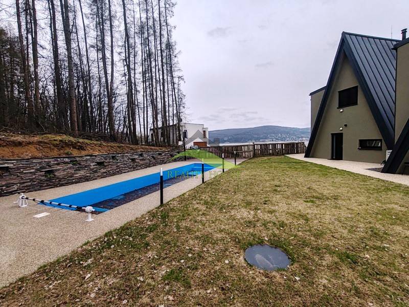 Ein Ferienhaus in der Straße Evy in Holčíkovce mit Pool und Rasen, umgeben von Wald.