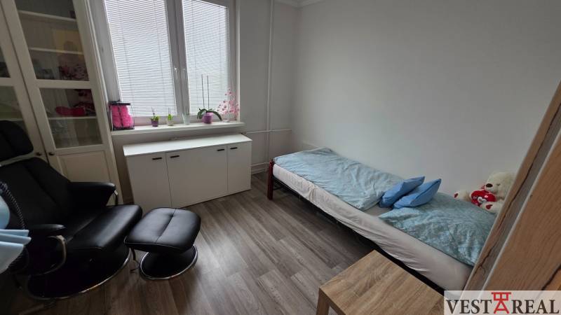 Ein Zimmer mit einem Sessel, einem Bett und einem Schrank, ein Boden mit Holzdekor, eine 3-Zimmer-Wohnung.