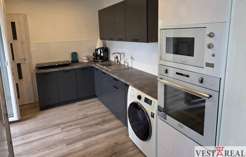 Küche in einer 3-Zimmer-Wohnung mit schwarzen Schränken und einem Boden in Holzoptik.