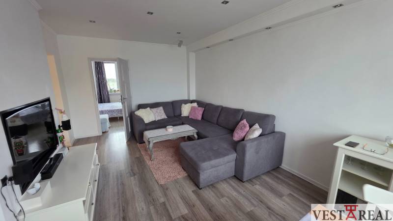 Wohnzimmer mit großem Sofa und Fernseher, in einer 3-Zimmer-Wohnung mit Holzboden-Dekor.