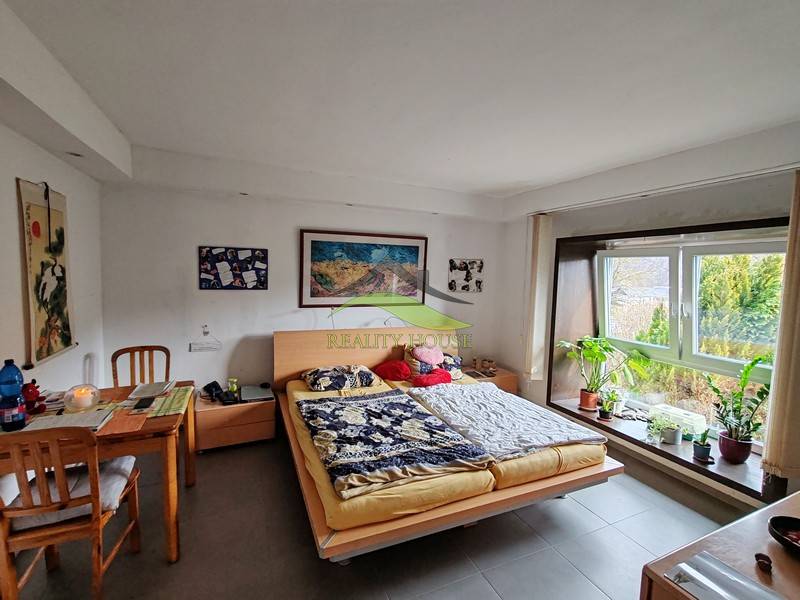 Ein Schlafzimmer in einem Einfamilienhaus mit einem Tisch und einem großen Fenster, Pflanzen auf der Fensterbank.