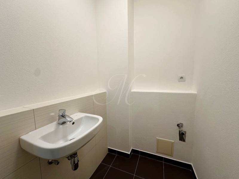 Toilette in einer 4-Zimmer-Wohnung mit weißem Waschbecken und schwarzen Fliesen.