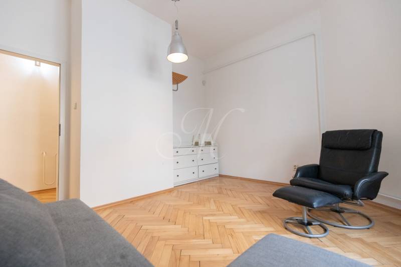 Innenraum einer 4-Zimmer-Wohnung mit Sessel, weißer Kommode und Boden in Holzoptik.