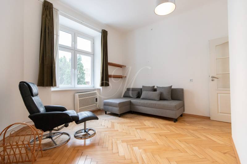 Helles Wohnzimmer mit Holzboden in einer 4-Zimmer-Wohnung, graues Sofa, Sessel.