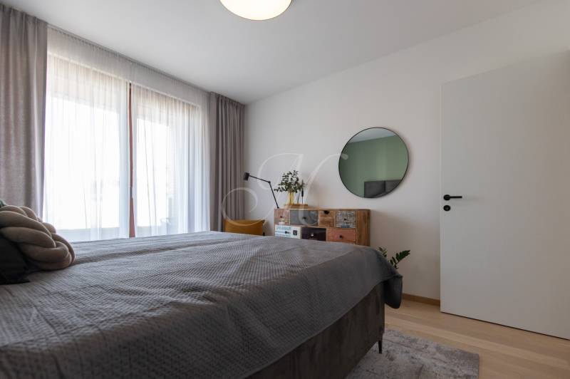 Schlafzimmer mit Bett, Spiegel und Kommode, auf einem Boden mit Holzdekor in einer 2-Zimmer-Wohnung.