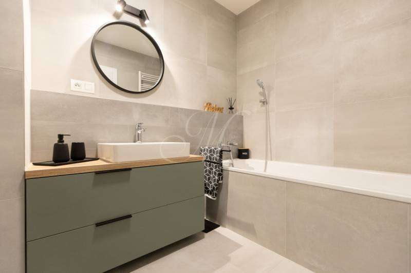 Badezimmer in einer 2-Zimmer-Wohnung mit Badewanne, Waschbecken und rundem Spiegel an der Wand.