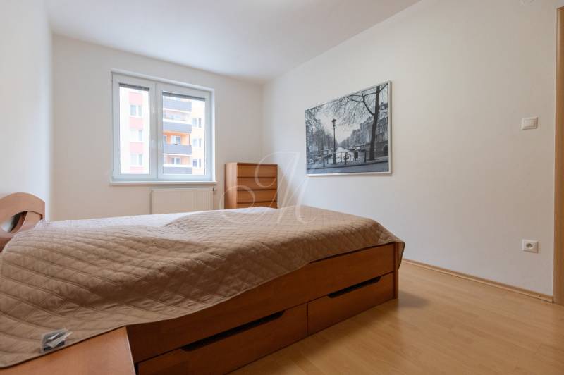 Schlafzimmer in einer 2-Zimmer-Wohnung mit eingebautem Bett und Bild an der Wand.