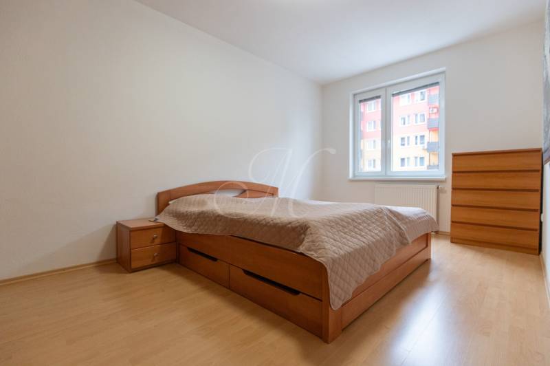 Ein Zimmer mit hellen Wänden, einem Doppelbett und einem Holzboden in einer 2-Zimmer-Wohnung.