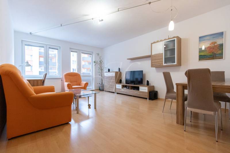 Wohnzimmer in einer Zweizimmerwohnung mit orangefarbenen Sesseln und einem Boden in Holzoptik.