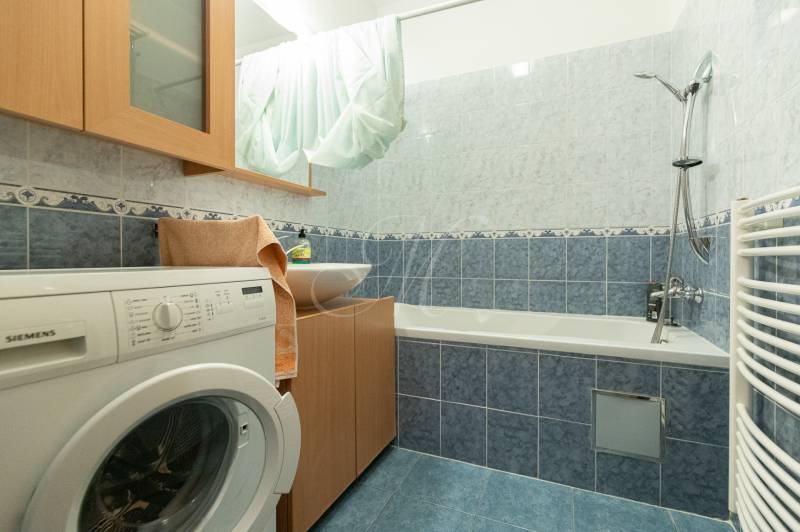 Badezimmer in einer 2-Zimmer-Wohnung mit Waschmaschine, Badewanne und blauen Fliesen.