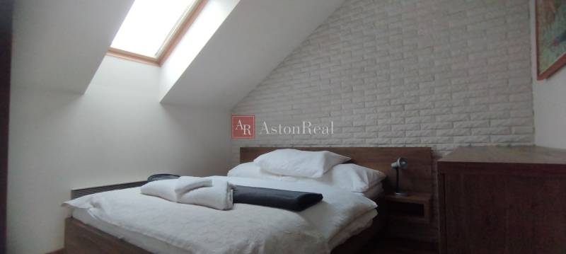 Schlafzimmer in einer 2-Zimmer-Wohnung mit Bett, Dachfenster und Ziegelverkleidung.
