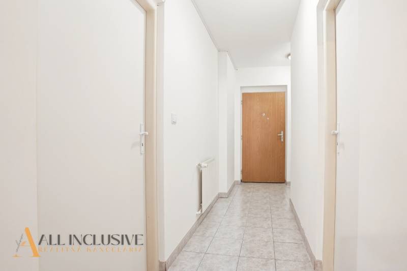 Flur mit weißen Wänden, Fliesenboden und Holztüren in einer Zweizimmerwohnung.