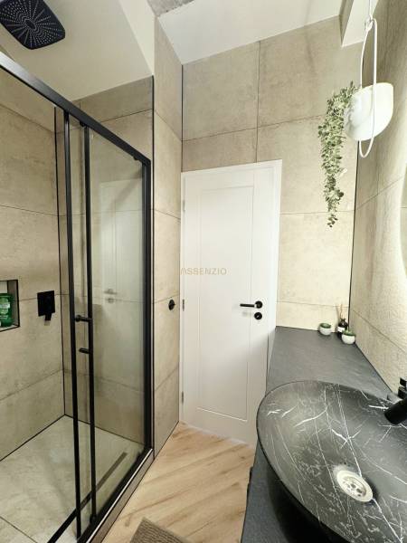 Badezimmer in einer 3-Zimmer-Wohnung mit schwarzem Waschbecken, Duschkabine und Boden mit Holzdekor.