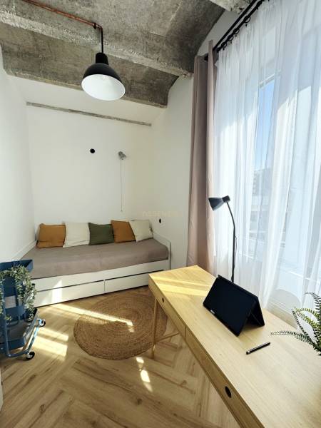 Ein Zimmer in einer 3-Zimmer-Wohnung mit Holzelementen, einem Bett und einem Schreibtisch mit einem Tablet.