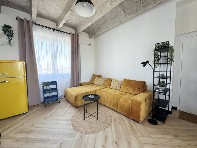 Wohnzimmer mit Holzboden, gelbem Sofa und Retro-Kühlschrank.
