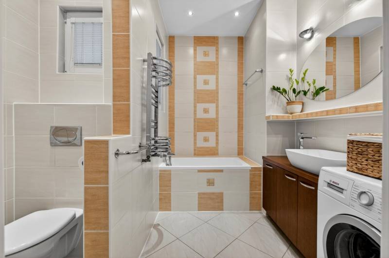 Badezimmer mit Badewanne, Waschmaschine, Waschbecken und dekorativen Fliesen in einer 3-Zimmer-Wohnung.