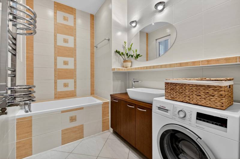 Badezimmer in einer 3-Zimmer-Wohnung mit Badewanne, Waschmaschine und braunen Fliesen.