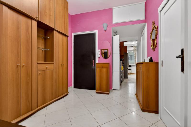 Geräumiger Flur einer 3-Zimmer-Wohnung mit Holzschränken und rosa Wänden.