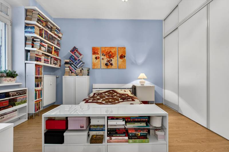 Ein Schlafzimmer mit Holzboden, Regalen voller Bücher und weißen Möbeln.