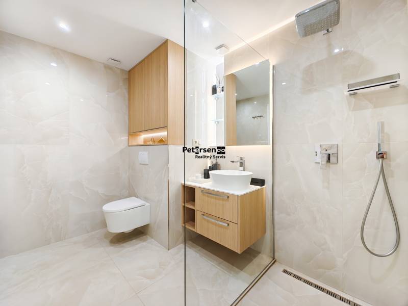 Badezimmer in einer 2-Zimmer-Wohnung mit begehbarer Dusche, weißem Waschbecken und Holzschränken.