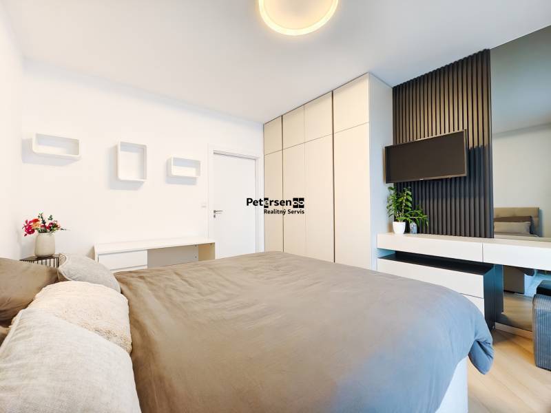 Schlafzimmer in einer 2-Zimmer-Wohnung mit Bett, Kleiderschrank und Fernseher an der Wand.