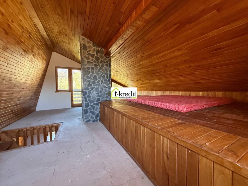 Das Dachgeschoss der Hütte mit Holzelementen und einem steinernen Kamin erinnert an einen gemütlichen Entspannungsraum.