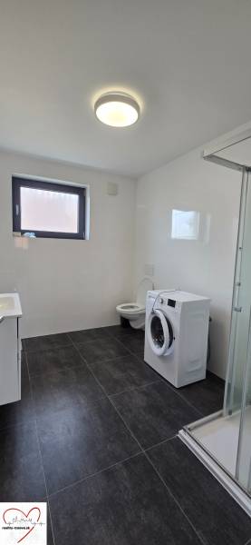 Badezimmer in einer 3-Zimmer-Wohnung mit Duschkabine, Waschmaschine und schwarzen Fliesen.