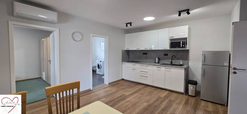 Küche mit weißen Schränken und Geräten in einer 3-Zimmer-Wohnung, Boden mit Holzdekor.