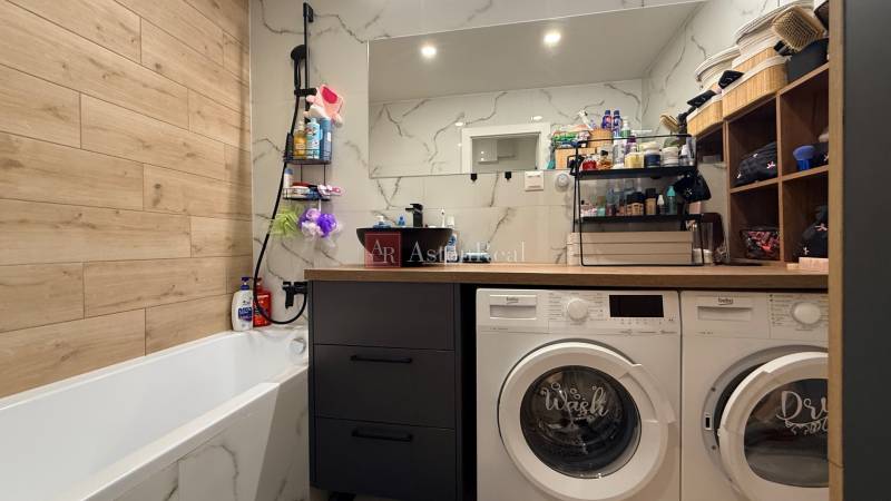 Badezimmer mit Dusche und Waschmaschine in einer 4-Zimmer-Wohnung, Boden mit Holzdekor.